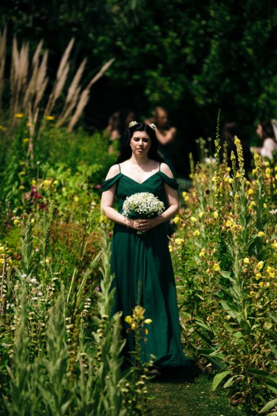 Bridesmaids in green walk through the flowers down the aisle