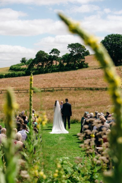 Bride and groom facing field farm guests in background