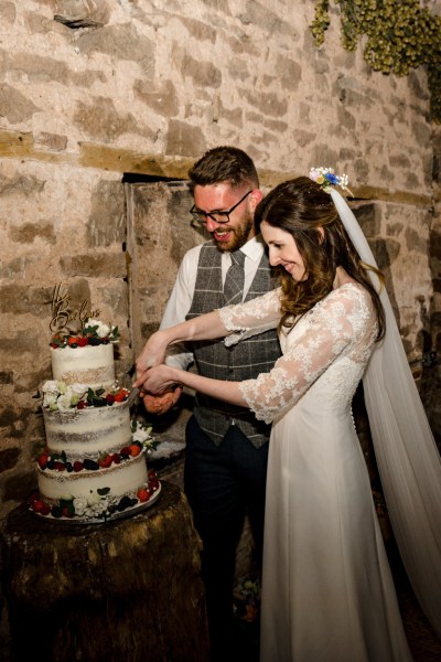 Bride and groom cut the wedding cake covered in fruit