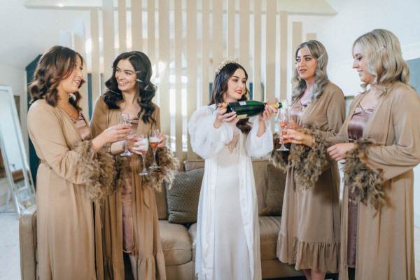 Bride pours champagne or prosecco into wine glasses foe bridesmaids