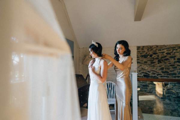 Bridesmaid helps bride with the back of her dress