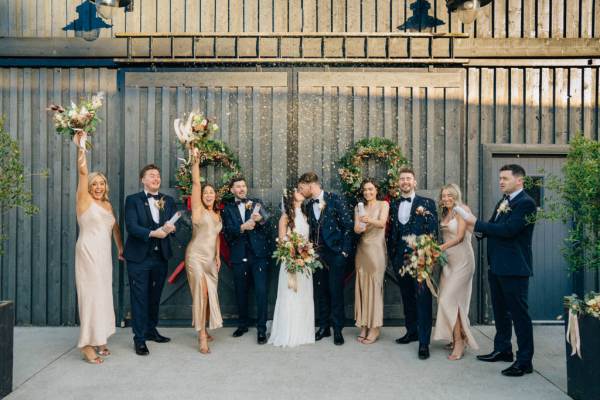 Bride groom bridesmaids groomsmen in front of barn door exterior couple kiss