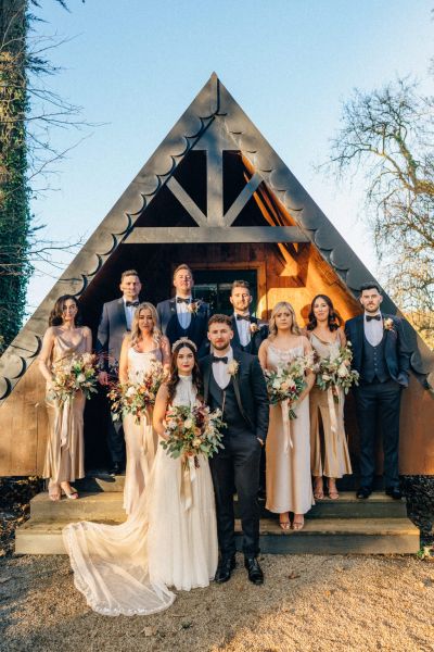 Bride and groom in front of cabin sunset with groomsmen bridesmaids family members