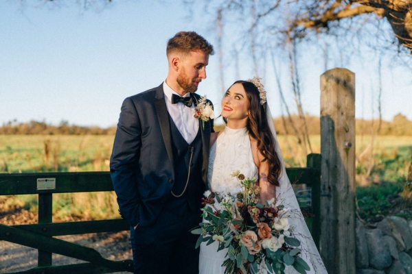 Bride and groom standing in front of fence on farm sunset