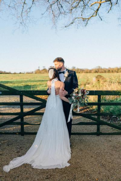 Bride and groom standing in front of fence on farm sunset kiss on the forehead