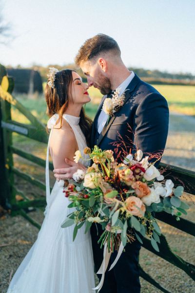 Bride and groom standing in front of fence on farm sunset facing each other