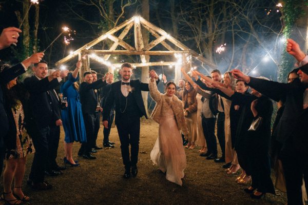 Guests outside in forest setting with bride and groom sparklers lit