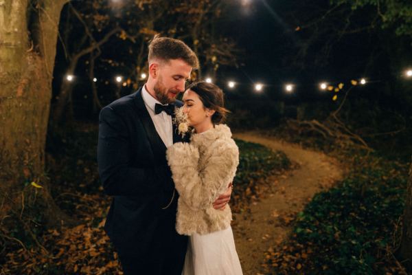 Bride and groom warm coat embrace hug on pathway to wedding venue