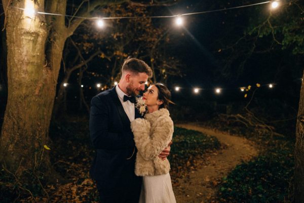 Bride and groom warm coat embrace hug on pathway to wedding venue