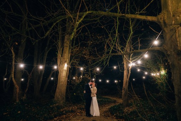 Bride and groom warm coat embrace hug on pathway to wedding venue