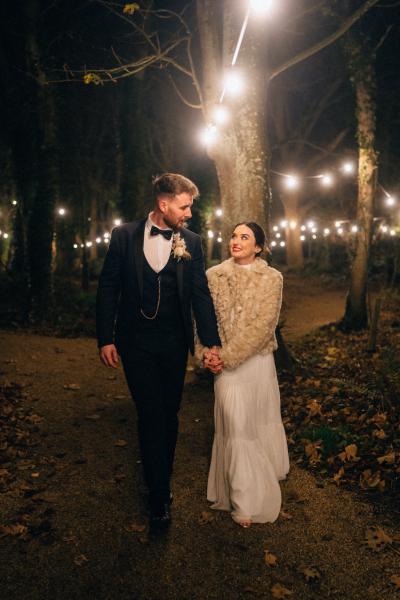 Bride and groom warm coat embrace hug on pathway to wedding venue walking holding hands