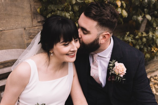 Groom kisses bride on the cheek as she smiles