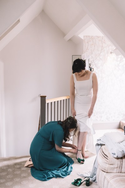 Bridesmaid puts green bridal heel shoe on bride bow ribbon