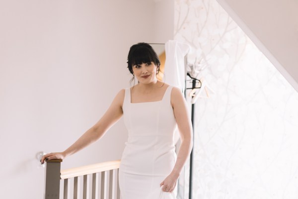 Bride stands as bridesmaid helps her get ready