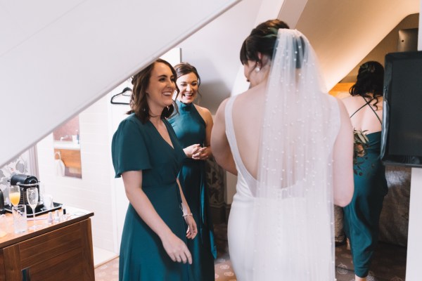 Two bridesmaids in green dresses and bride from behind veil detail