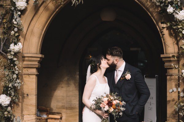 Bride and groom kiss at archway to church/venue