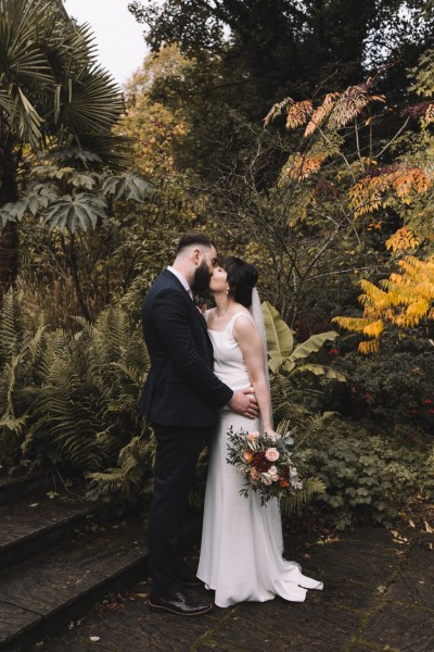 Bride and groom hold each other in garden and kiss