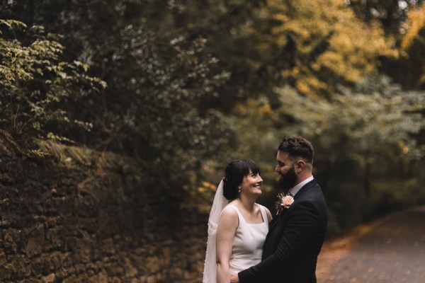 Bride and groom stand looking at each other in garden/park