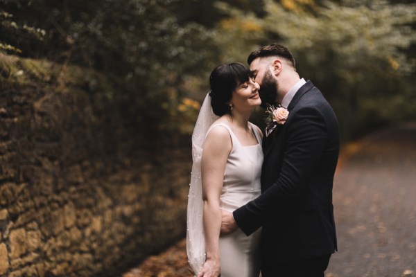 Groom kisses bride on pathway in park