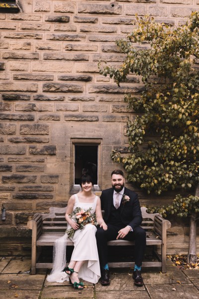 Bride and groom sit on bench together holding hands