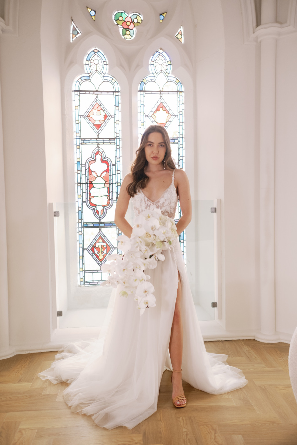 Charlotte Mills Studio Collection | OneFabDay.com | Bride stands in front of tinted church window holding white flowers smiling