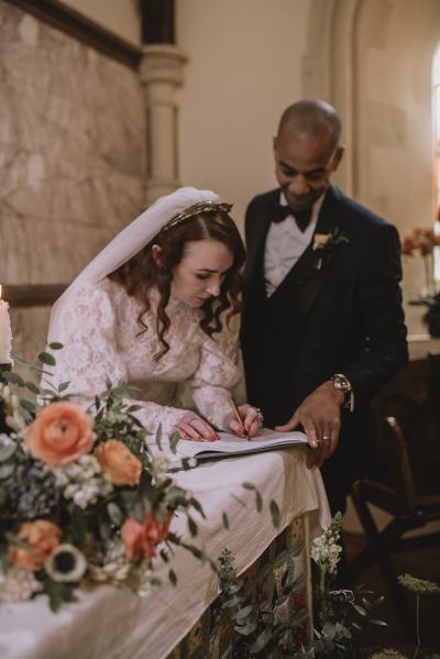 Bride and groom signing marriage wedding cert orange flowers roses in shot