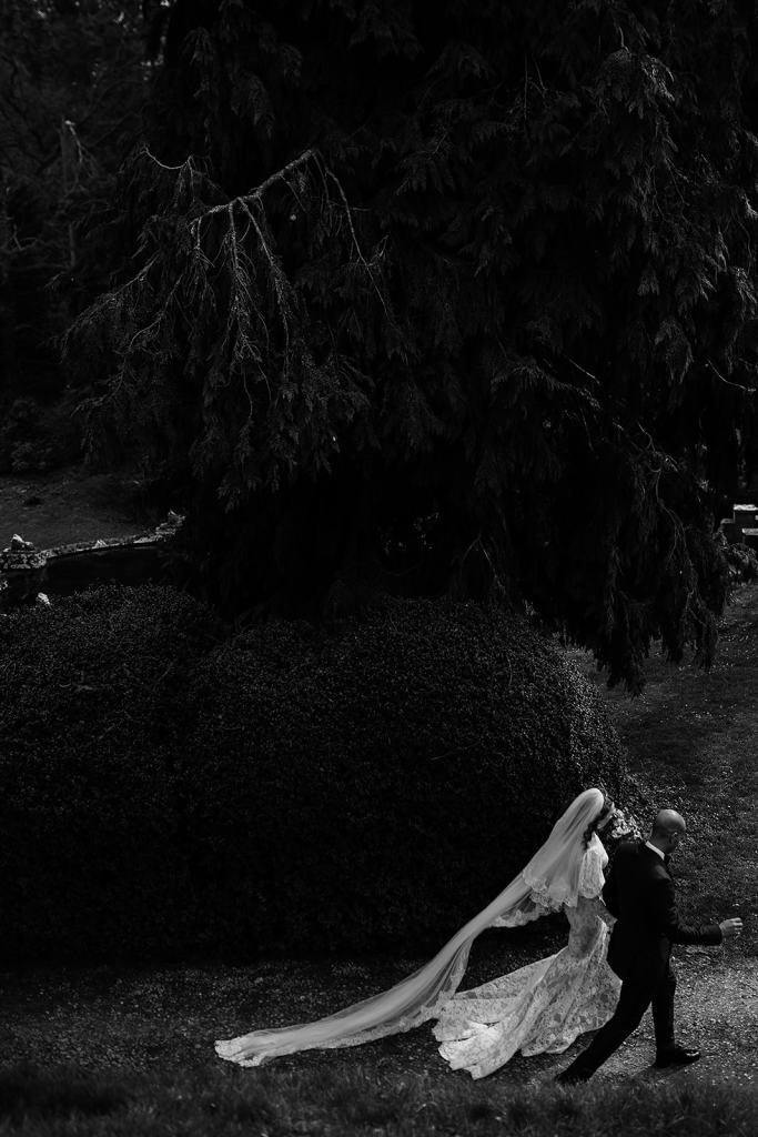 Bride and groom walk in forest park dark photography holding hands