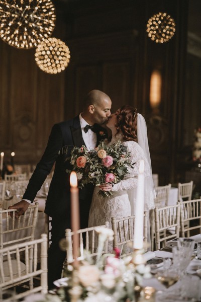 Bride and groom kiss in empty ballroom dining room setting