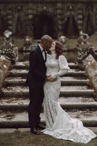 Bride and groom walk down the steps to wedding venue kissing embracing