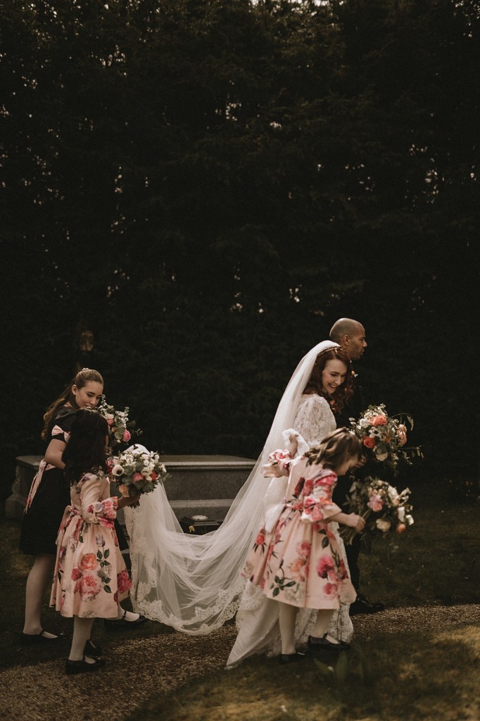 Bride groom bridesmaid holding brides dress train veil detail as they walk