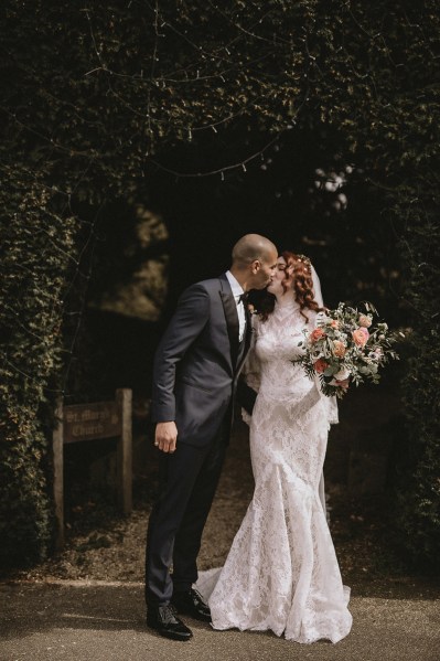 Bride and groom kiss as she holds bouquet of flowers