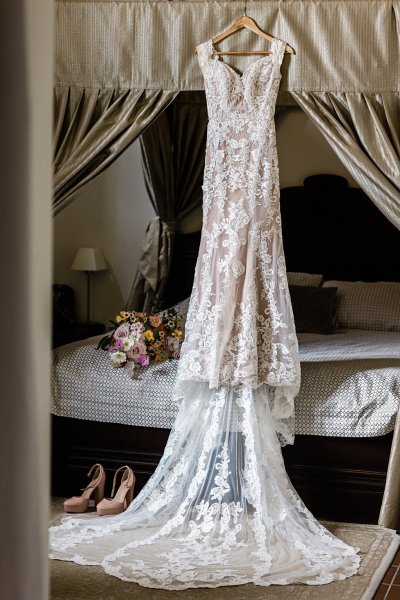 Bride in bridalwear looking at bridal gown dress lace detail hanging up