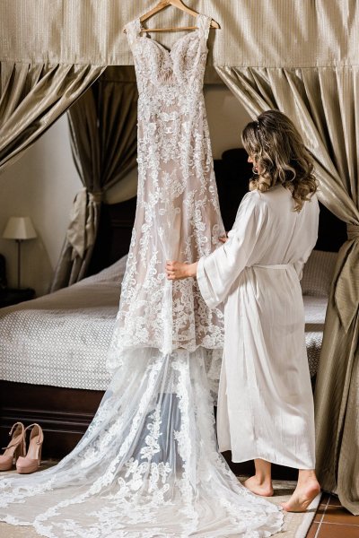 Bride in bridalwear looking at bridal gown dress lace detail hanging up