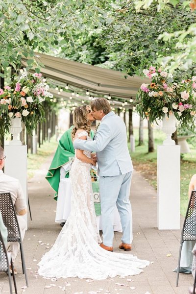 Bride and groom kiss in front of guests at alter in front of celebrant during ceremony