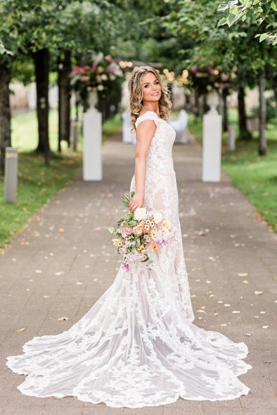 Bride holds bouquet flowers colourful dress gown lace from behind