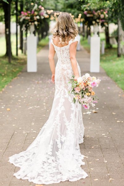 Bride holds bouquet flowers colourful dress gown lace from behind