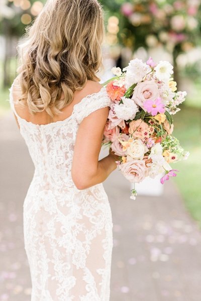 Back of brides dress lace detail she holds bouquet colourful flowers