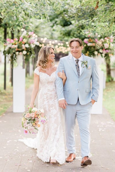 Bride and groom hold hands in forest park setting bouquet in hand flowers in background