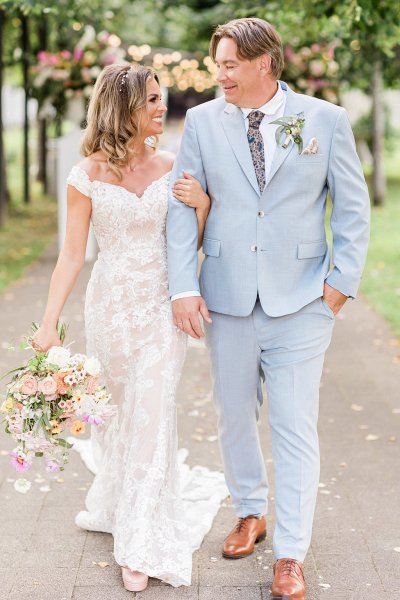 Bride and groom hold hands in forest park setting bouquet in hand flowers in background