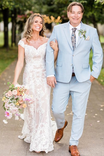 Bride and groom hold hands in forest park setting bouquet in hand flowers in background