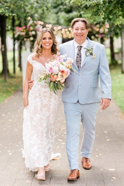 Grooms arm around brides waist in forest park pathway they smile