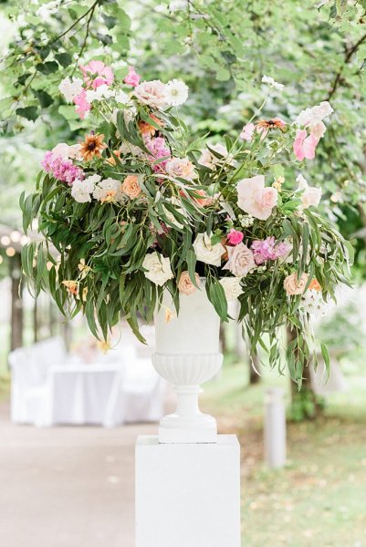 Colourful flowers in vase on white pillar in forest setting