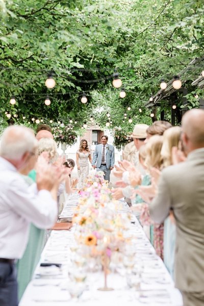 Bride and groom raise their wine glasses red and white guests colourful floral flowers bouquet table