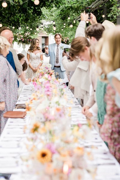 Bride and groom raise their wine glasses red and white guests colourful floral flowers bouquet table