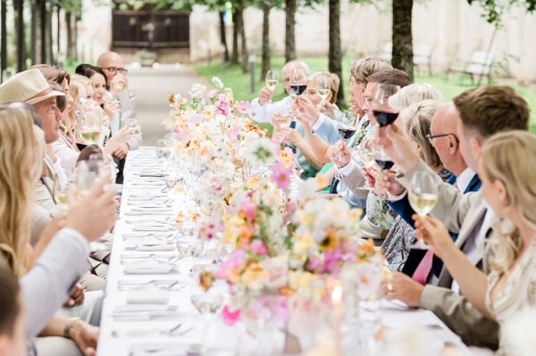 Bride and groom raise their wine glasses red and white guests colourful floral flowers bouquet table