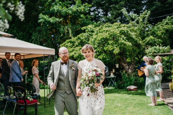 Bride and groom walk hand in hand in the sunshine garden grass