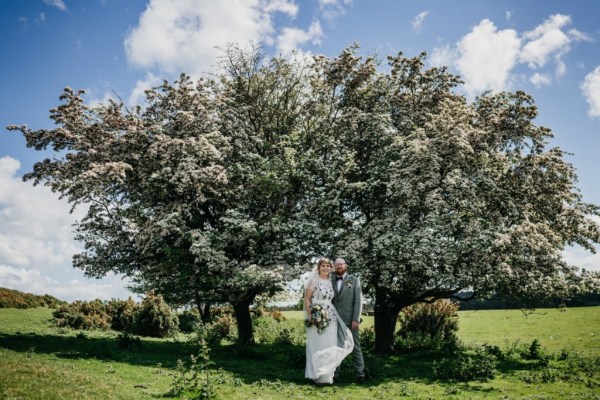 Bride laughs groom hugs her on grass forest setting tree