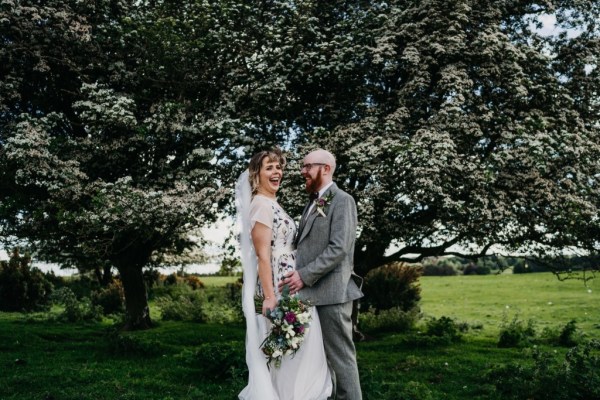 Bride laughs groom hugs her on grass forest setting