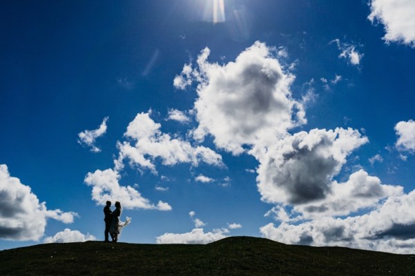 Couple bride and groom stand on cliff mountain blue sky in background clouds