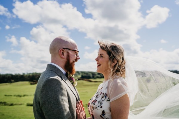 Bride and groom look at each other skyline in background wind blowing